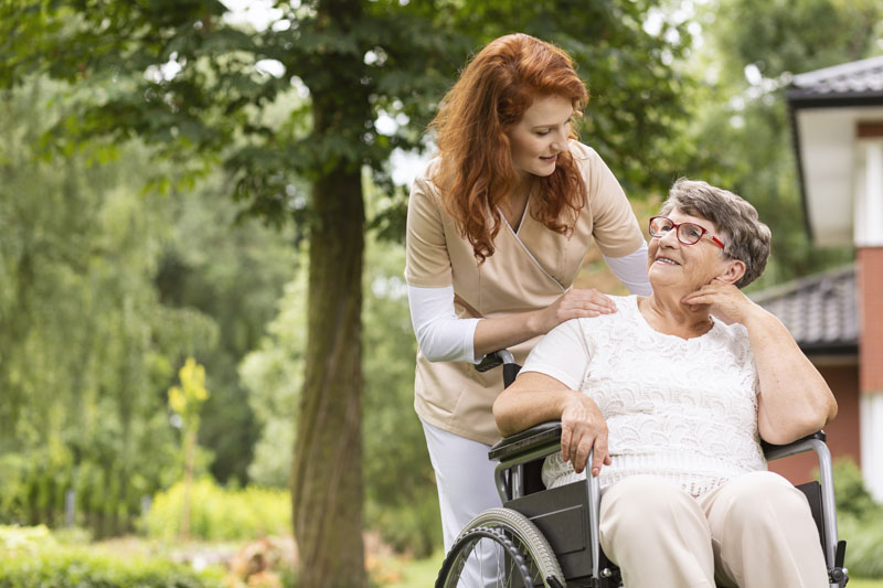 a female in home care staff helping an elderly woman in a wheelchair