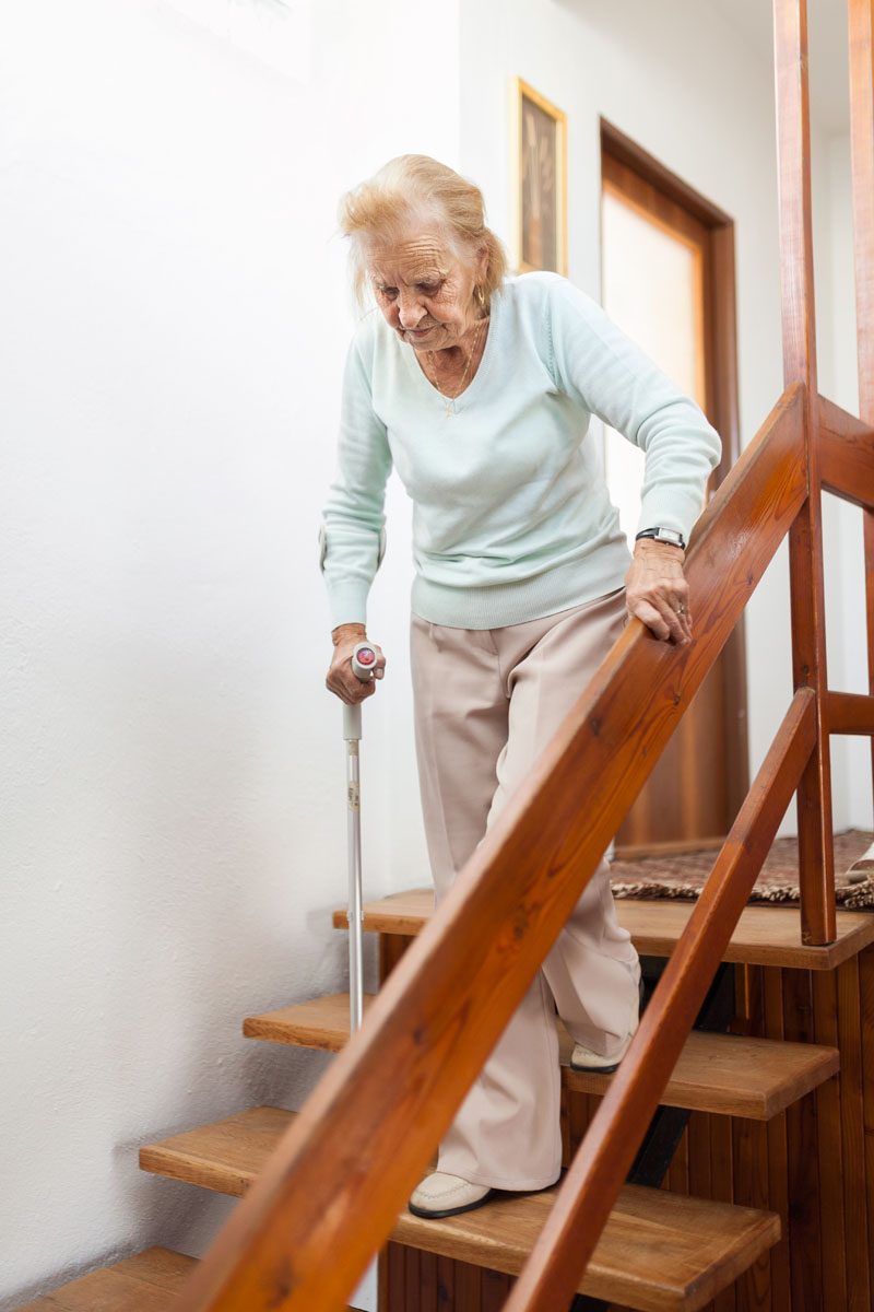 elderly woman at home using a cane to get down the stairs