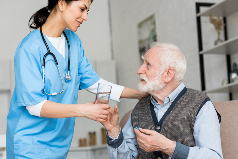 nurse giving glass of water to elderly man with dementia