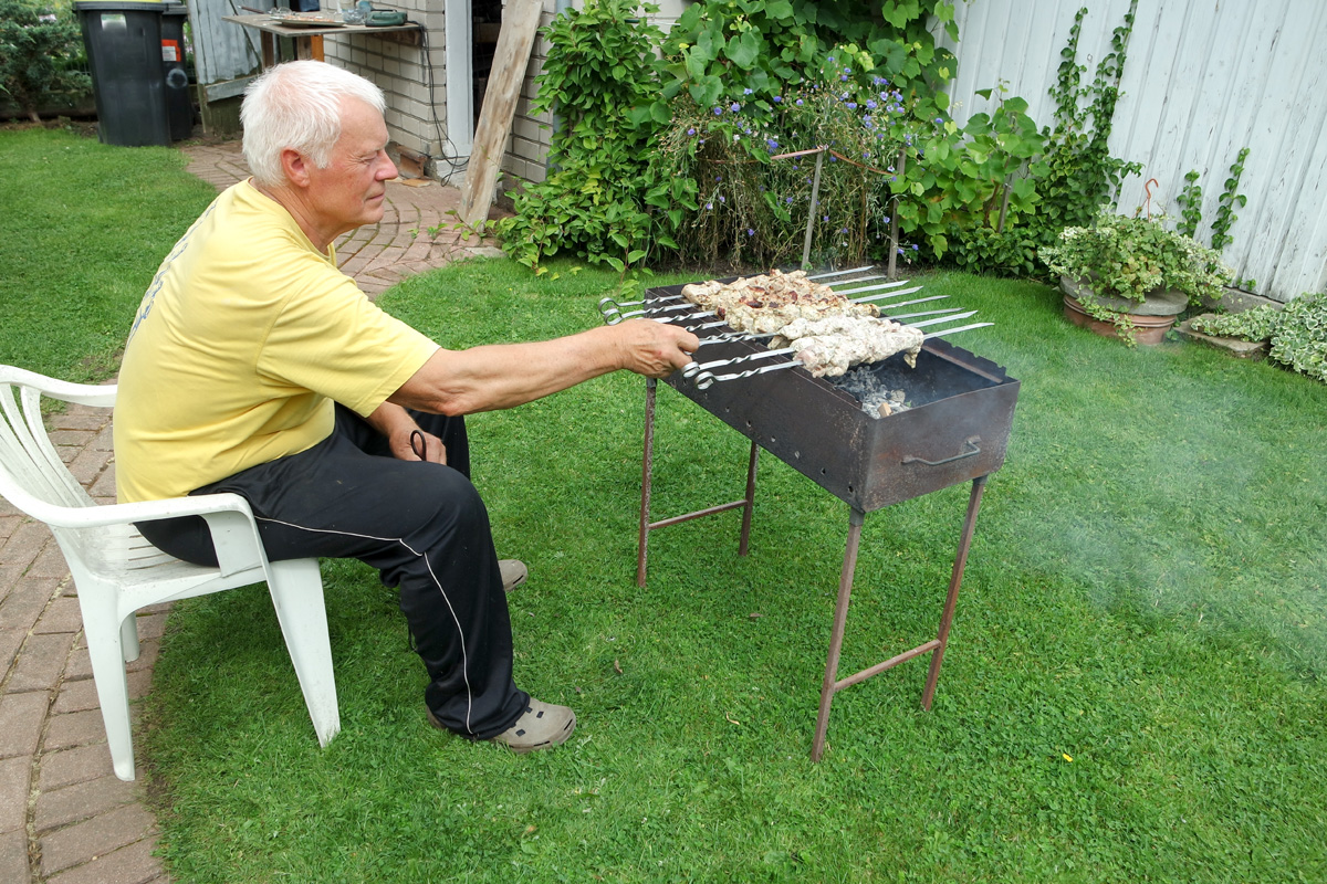 старший мужчина жарит мясо на заднем дворе