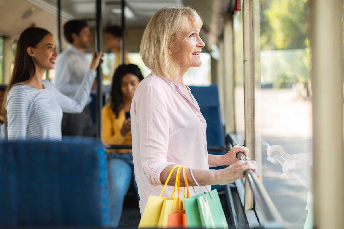 lächelnde, reife Frau, die den Bus hält und einkaufen geht